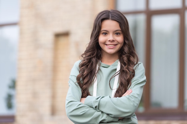 Confident teen girl happy smiling in casual hoodie keeping arms crossed blurry outdoors