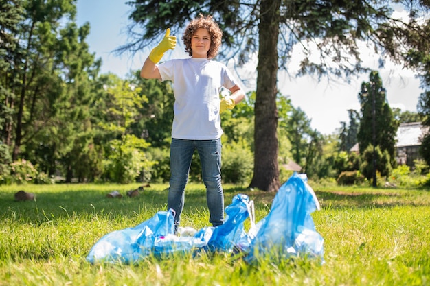 Confident teen standing near bags full with garbage