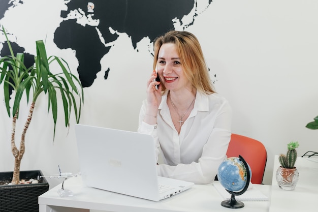 Confident travel agent using laptop in office over map for communication online