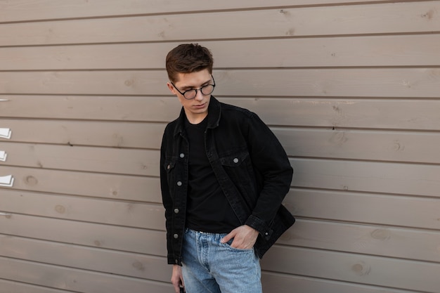 Confident trendy young man in fashionable youth denim clothes in stylish glasses