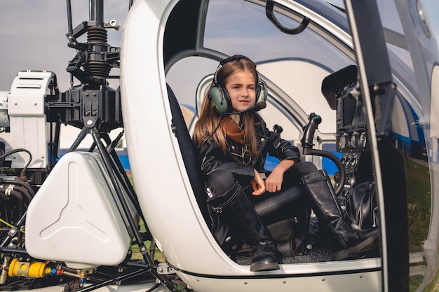 Confident tween girl in pilot headset sitting in helicopter cockpit