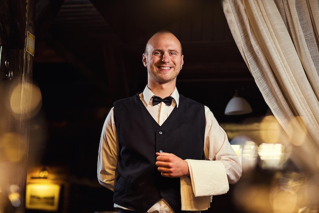 Confident waiter in uniform with a white towel served table in the restaurant before the feast