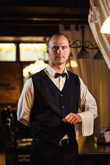 Confident waiter in uniform with a white towel served table in the restaurant before the feast