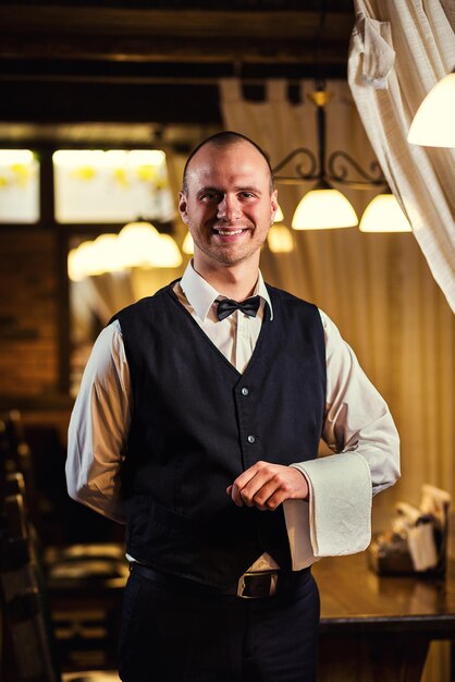 Confident waiter in uniform with a white towel served table in the restaurant before the feast