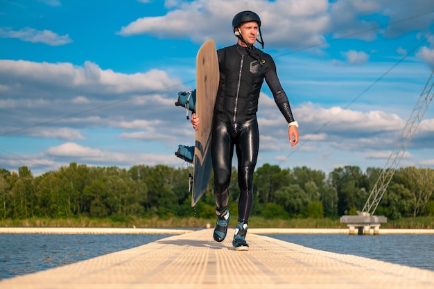 Confident wakeboarder walking with board along pier after training