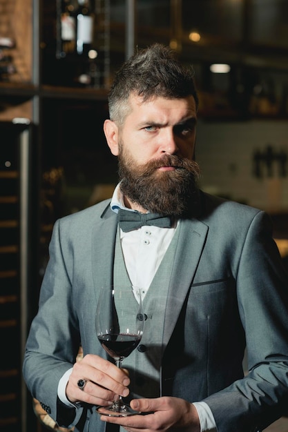 Confident winemaker in romantic atmosphere of cigar club. cigar club, serious winemaker with glass in business suit.