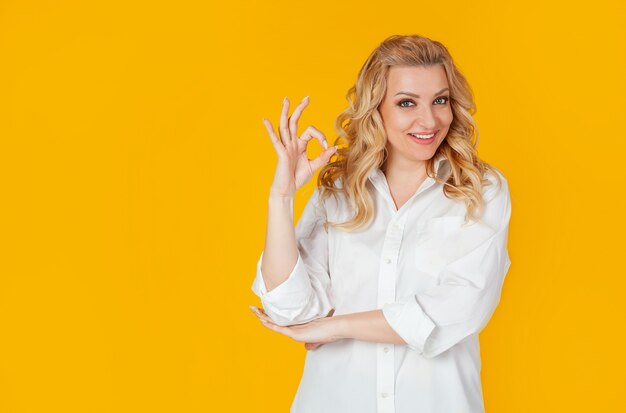 Fiduciosa donna vestita con una camicia bianca, sorridendo ampiamente, mostrando bene, bene, gesto, buon umore