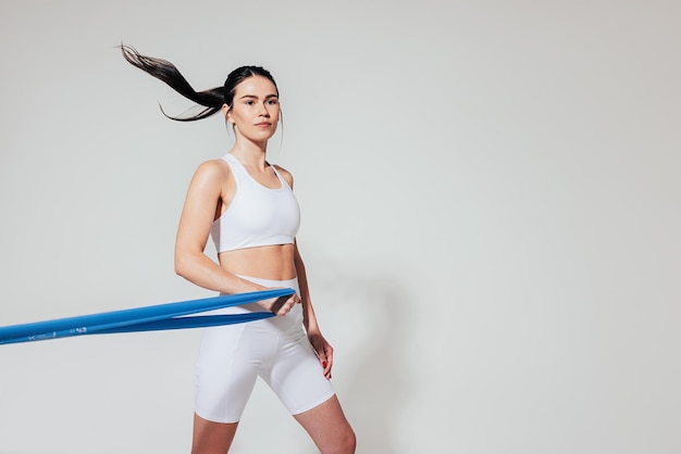 Confident woman in fitness wear with resistance band over white backdrop