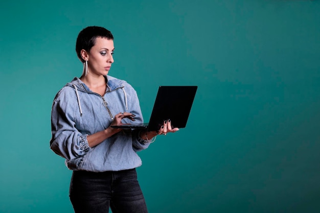 Confident woman holding laptop computer typing business strategy working at financial project in studio with isolated background. Positive female collaborating with remote colleagues