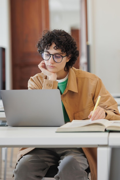 Confident woman in library or coworking works laptop online female student reads book