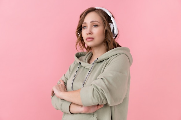 Confident woman listen music headphones Caucasian female enjoy podcast or audio books dressed oversize hoodie pink background close up portrait