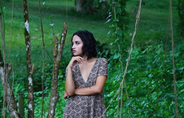 Confident woman looking away while standing against plants at park