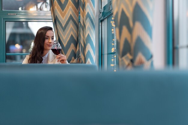 Confident woman. Pensive attractive elegant woman sipping wine and posing at restaurant and looking through window