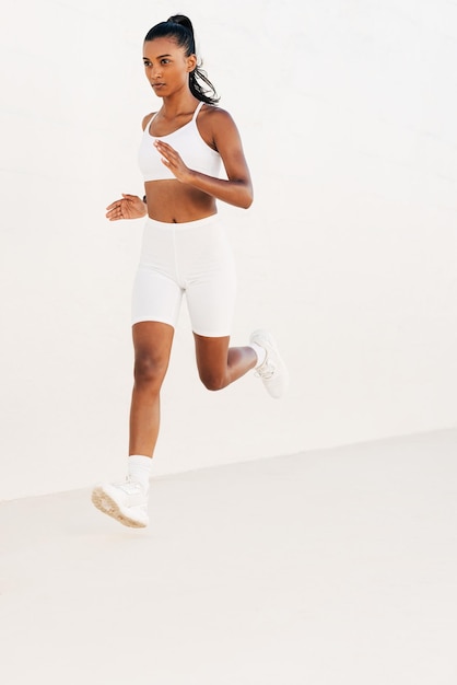 Confident woman sprinting against a white wall Slim jogger in white fitness attire running outdoorsx9xA