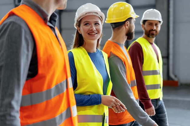 confident woman wearing hard hat and vest talking to her colleagues while walking around warehouse