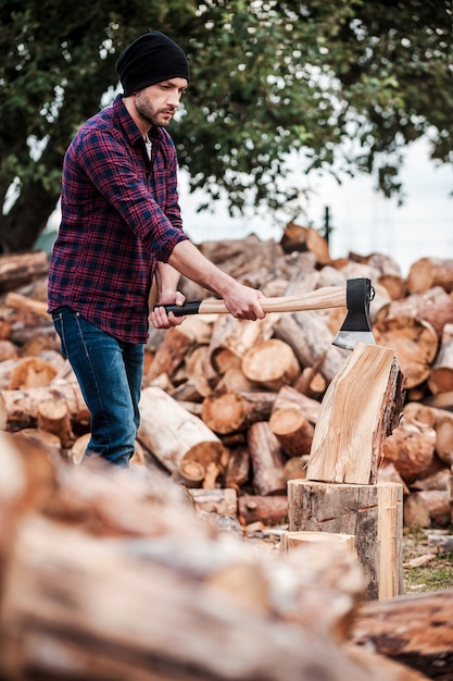 Confident woodworker. Serious young forester cutting log while standing outdoors