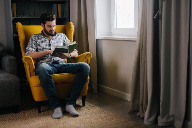 창가에서 책을 읽는 수염을 기른 자신감 있는 젊은 성인 남자 일상 생활의 개념