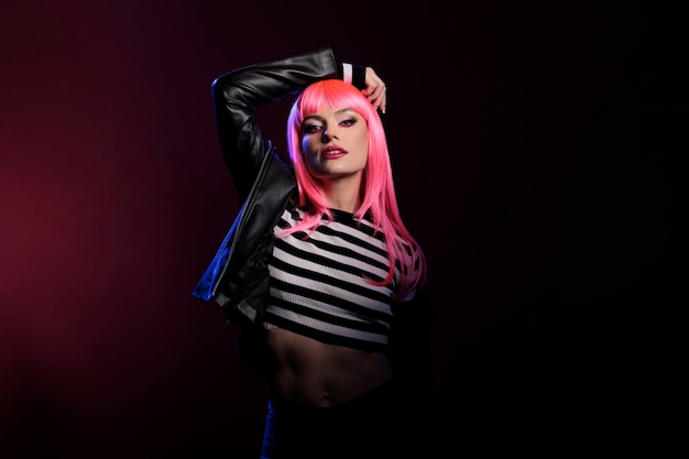 Confident young adult posing in dark pink shadow over background, wearing rocker leather jacket to be stylish and trendy. Modern attractive person with punk fashion style looking at camera.