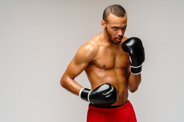 Confident young African boxer in boxing gloves standing over light grey wall