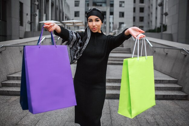 Confident young arabian woman hold colorful shopping bag and look at camera