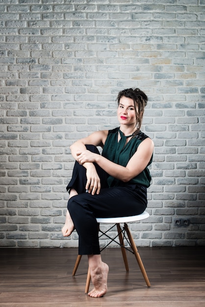 Confident young beautiful woman sits on white modern chair