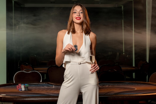 Confident young brunette with betting chips and glass of champagne in casino