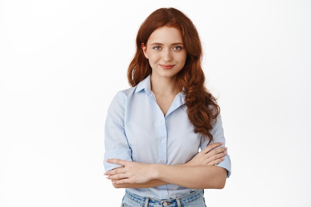 Confident young business woman professional, cross arms on chest and smiling determined, standing in office blouse against white background, staring ready.