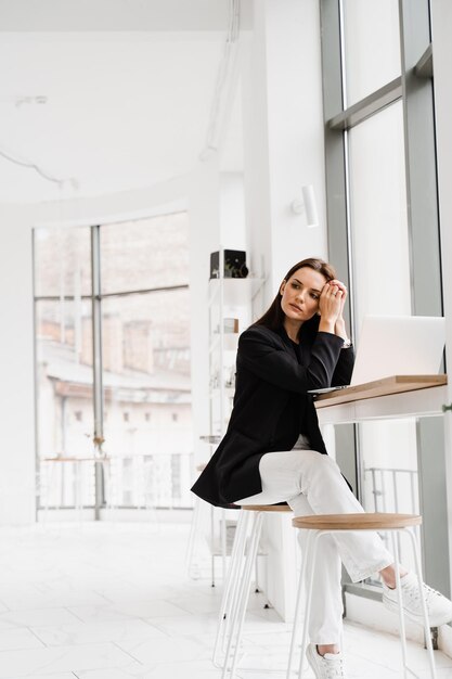 Confident young business woman working online with team on laptop on startup project Attractive girl programmer with laptop is working online in white cafe