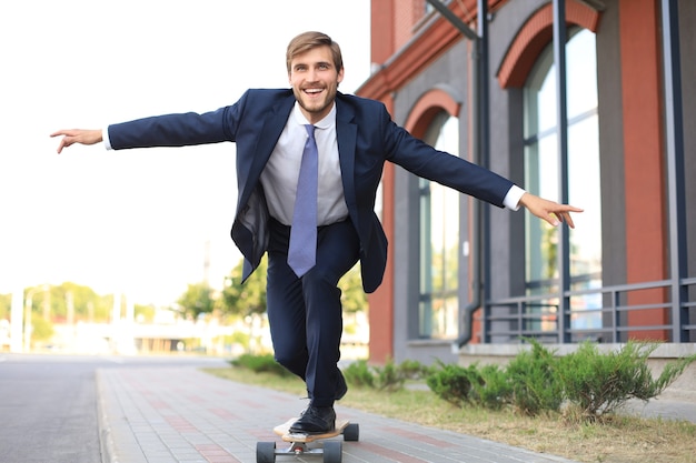 Fiducioso giovane uomo d'affari in tailleur su longboard che si affretta nel suo ufficio, per strada in città.