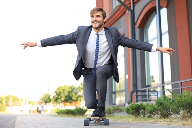 Confident young businessman in business suit on longboard hurrying to his office, on the street in the city.