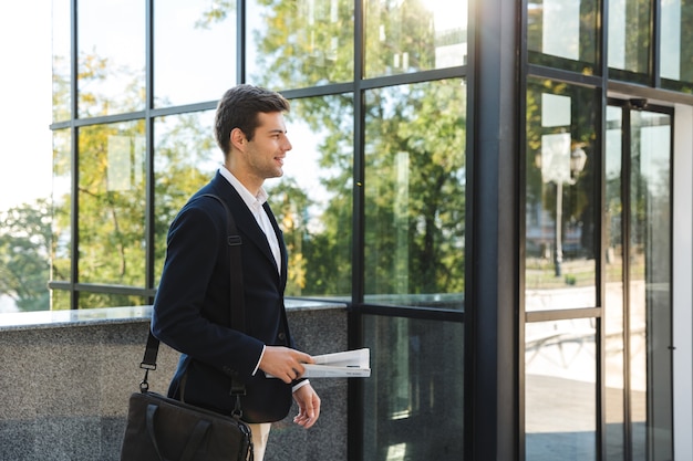 Confident young businessman carrying bag, walking outdoors