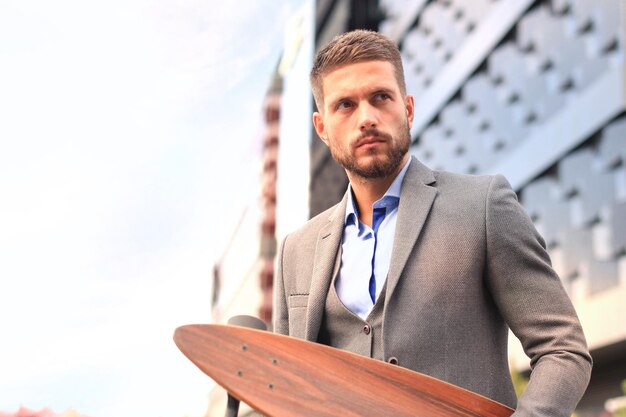 Confident young businessman walking on the street using longboard