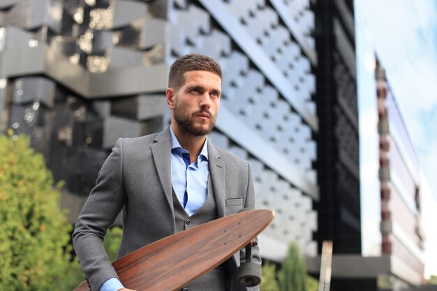 Confident young businessman walking on the street, using longboard.