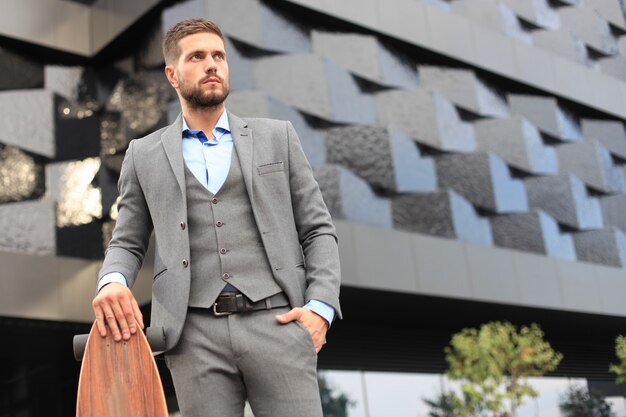 Confident young businessman walking on the street, using longboard.