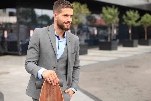 Confident young businessman walking on the street, using longboard.