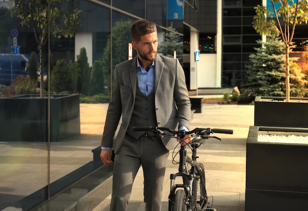 Confident young businessman walking with bicycle on the street in town