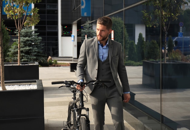 Confident young businessman walking with bicycle on the street in town.