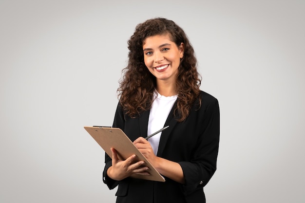 Photo confident young businesswoman writing on clipboard