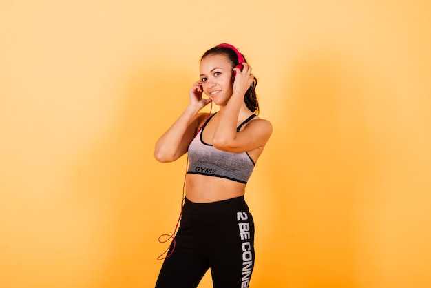 Confident young fit african sportswoman listening to music with a headphones over yellow background