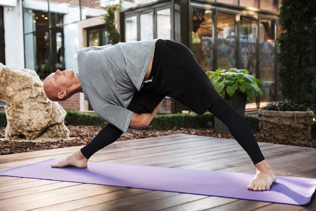 Confident young fitness man doing stretching yoga exercises on a mat outdoors