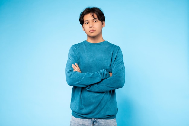 Confident young guy with arms crossed blue background