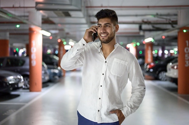 Confident young handsome man walking along the parking lot while talking on the phone after having p...