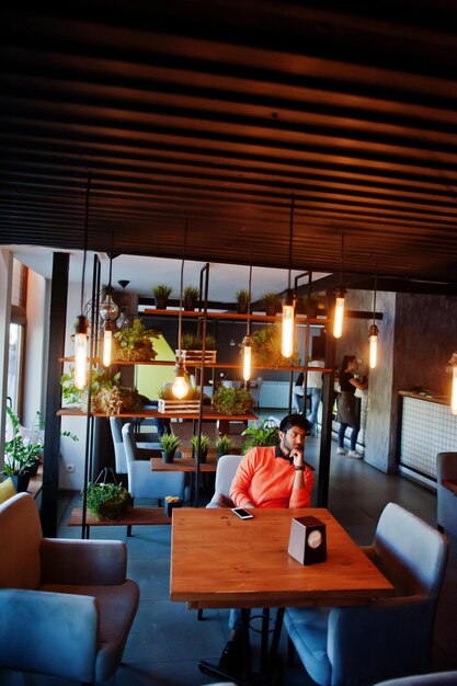 confident young indian man in smart casual wear like orange sweater sitting at cafe