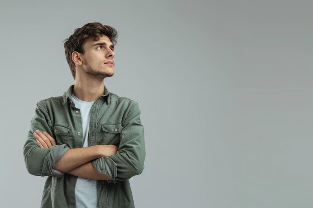 Foto giovane fiducioso in camicia verde casuale che guarda lontano in piedi con le braccia incrociate isolato sul grigio