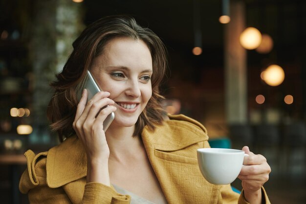 Confident young man in casual shirt sitting in armchair and looking away while talking by phone in m