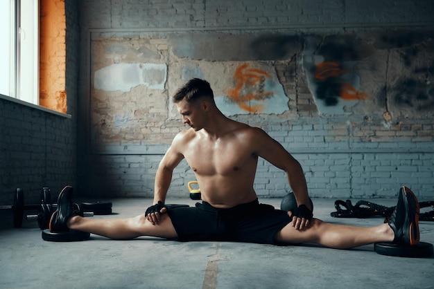 Photo confident young man doing the splits while exercising in gym