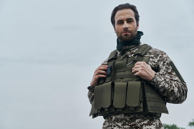 軍服を着た自信のある若い男が屋外に立ってカメラを見ている