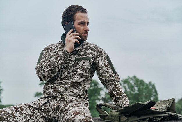 外に座って携帯電話で話している軍服を着た自信のある若い男性