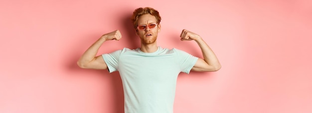 Confident young man with red hair wearing summer sunglasses and tshirt showing strong and fit body m