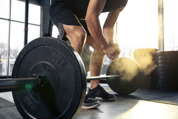 Confident. Young muscular caucasian athlete training in gym, doing strength exercises, practicing, work on his upper body with weights and barbell. Fitness, wellness, healthy lifestyle concept.